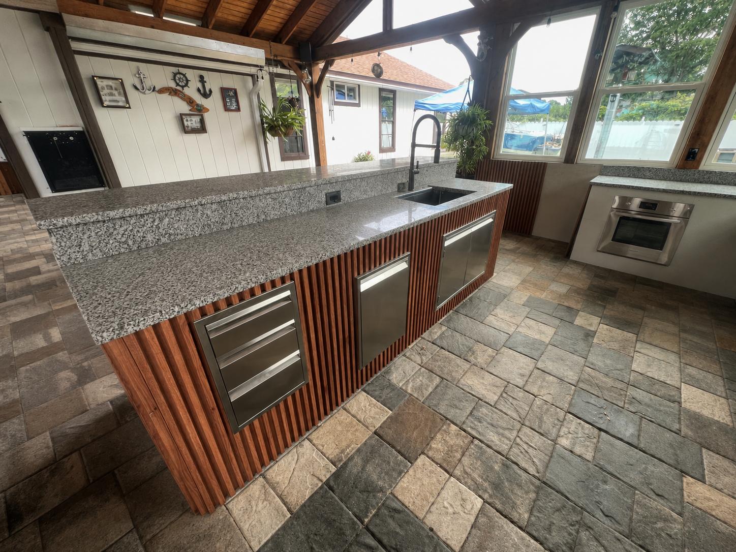 Isla de cocina exterior revestida en panel de lamas de madera WPC con fregadero