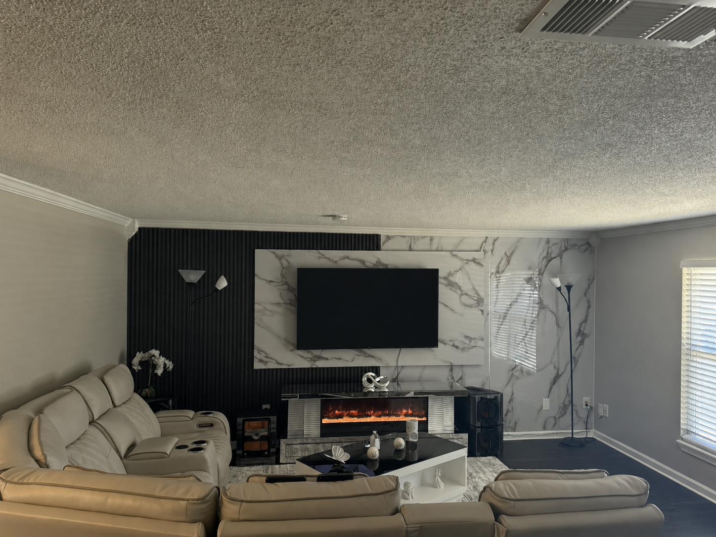 Sala con panel de televisor en mármol PVC, lamas negras y chimenea eléctrica